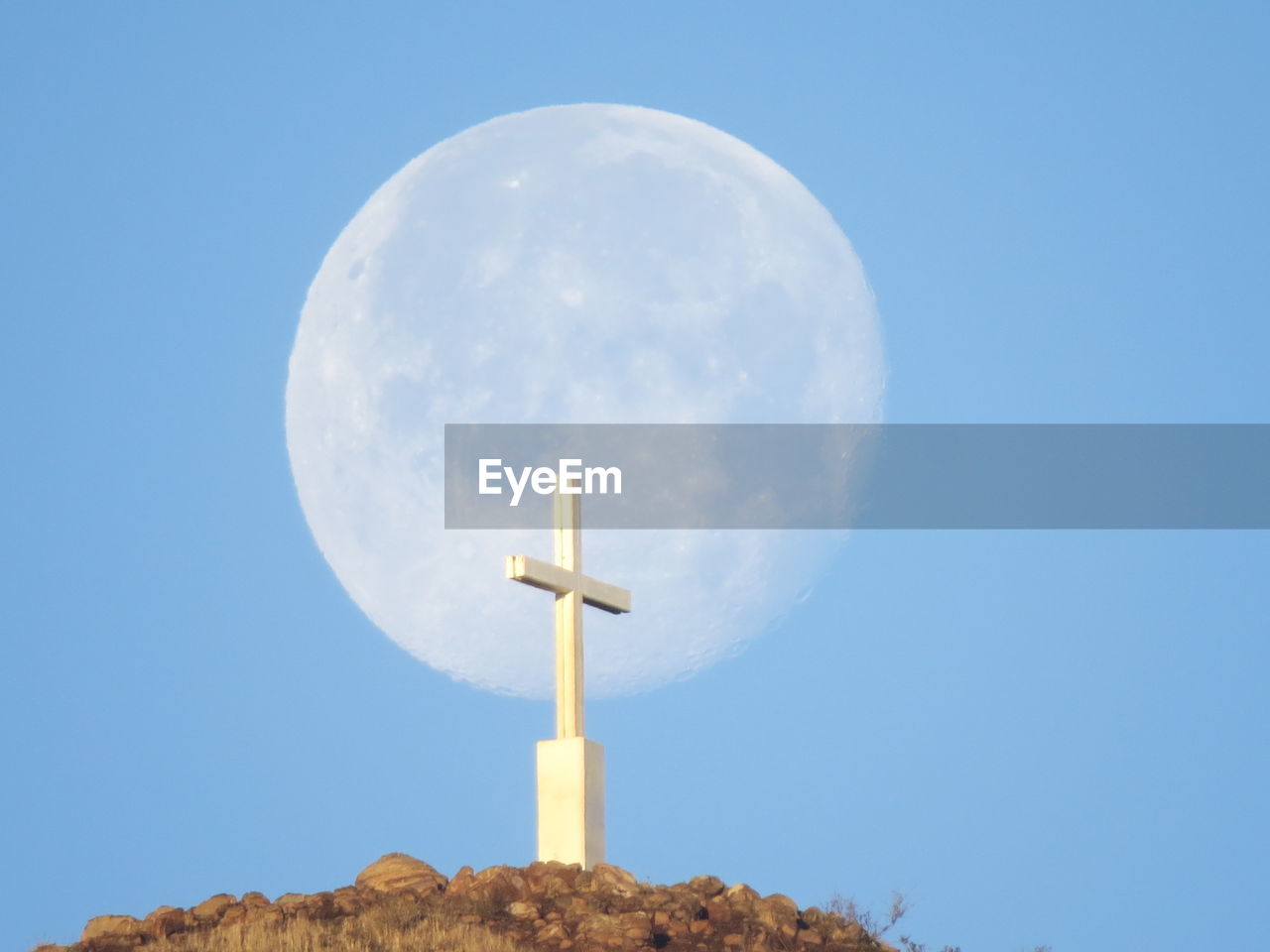 Low angle view of cross against blue sky with setting moon. 
