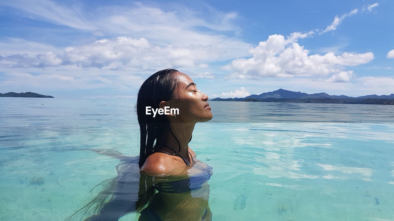 Side view of woman swimming in sea with eyes closed during summer