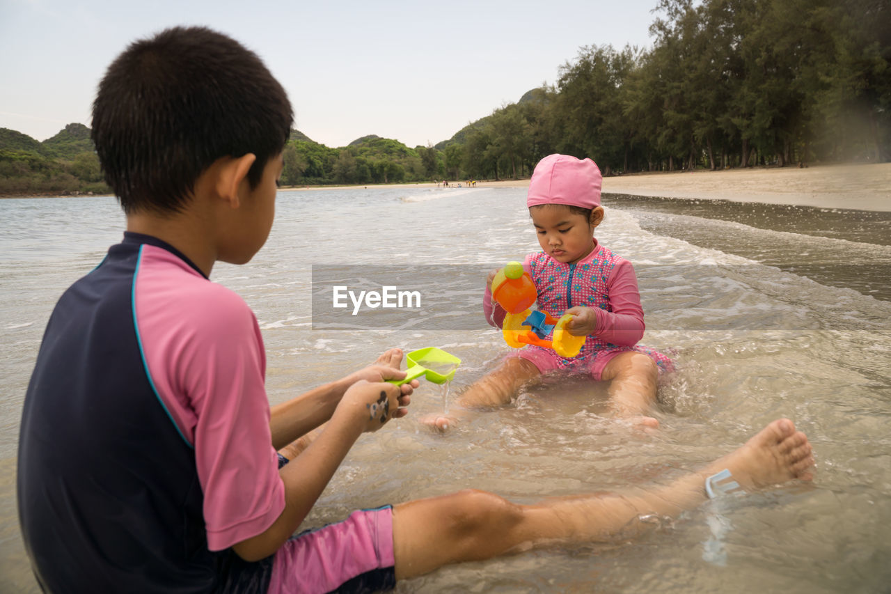 Girl and brother playing with toys at beach