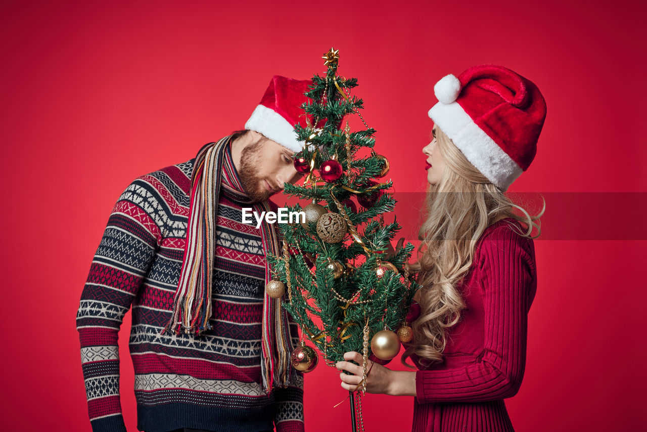 MIDSECTION OF MAN WITH CHRISTMAS TREE AGAINST RED WALL