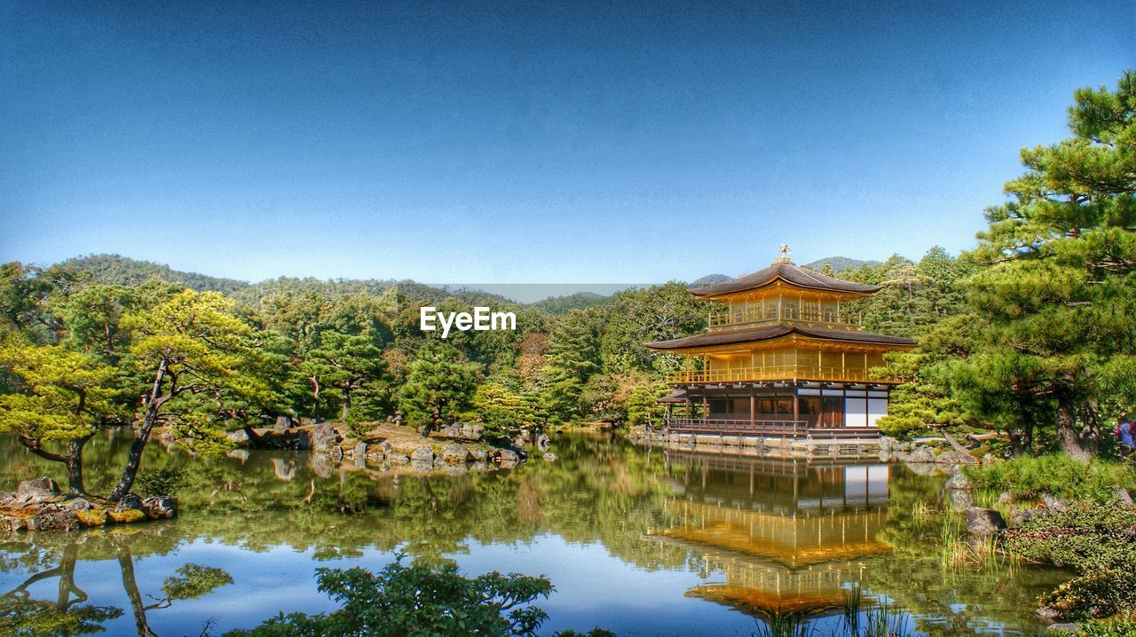 Reflection of kinkaku-ji and trees in lake against clear sky
