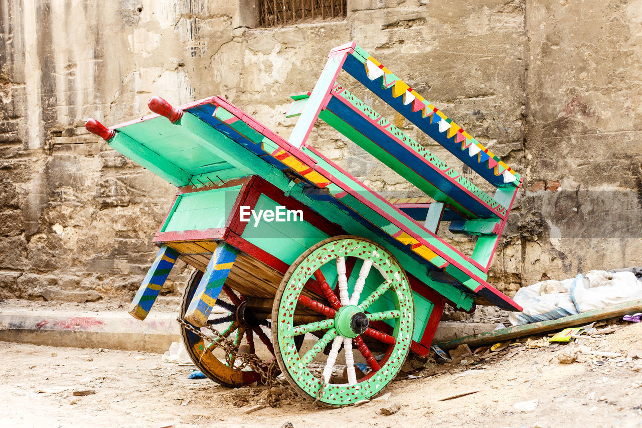 Multi colored push cart on sidewalk against wall