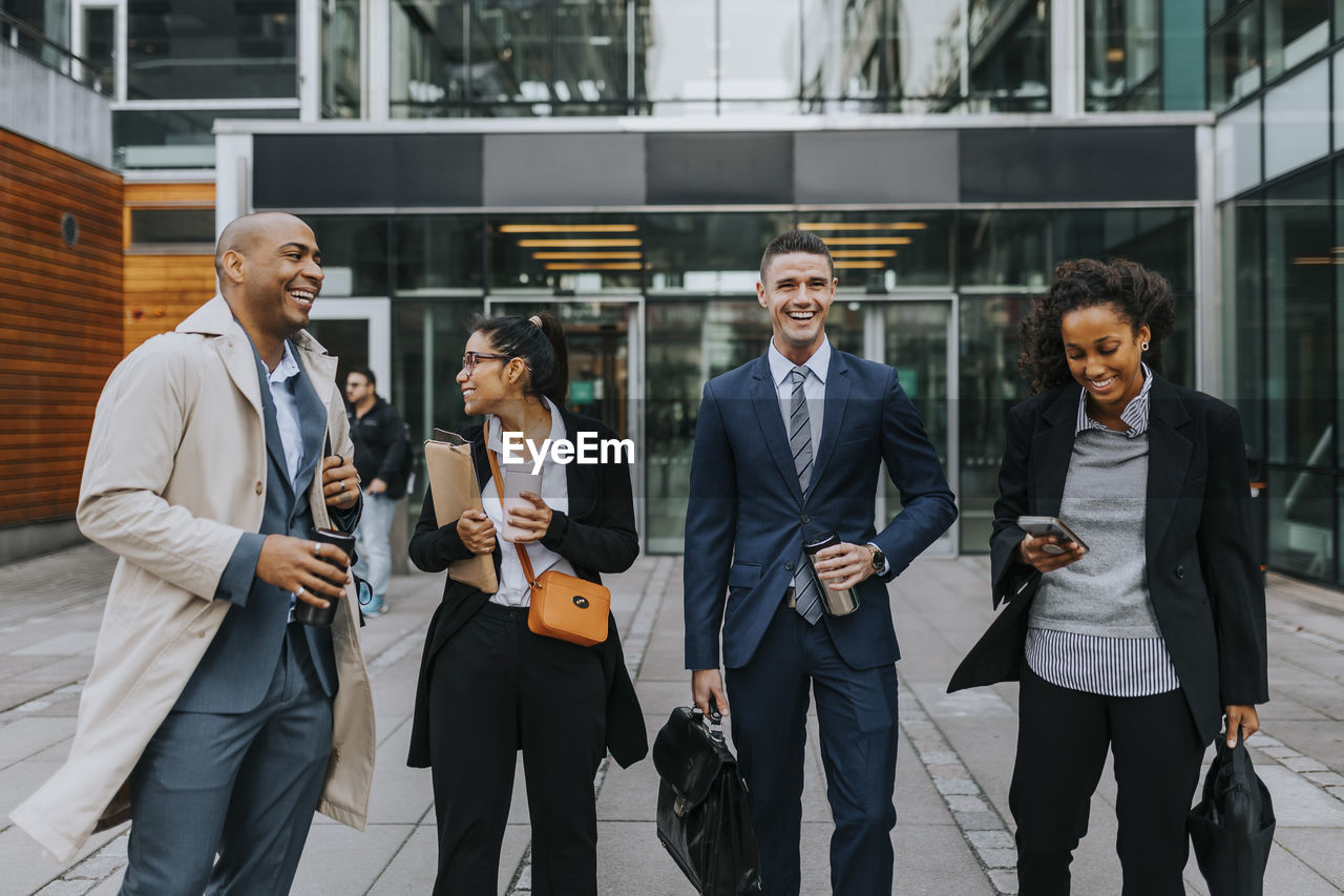 Happy male and female corporate professionals standing in front of office building