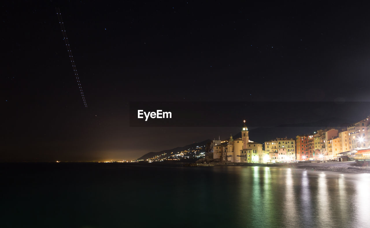 ILLUMINATED CITYSCAPE BY SEA AGAINST SKY