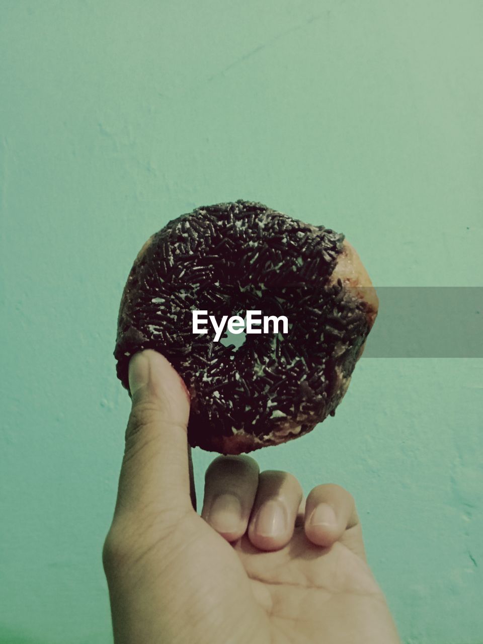 Close-up of hand holding donut against white background