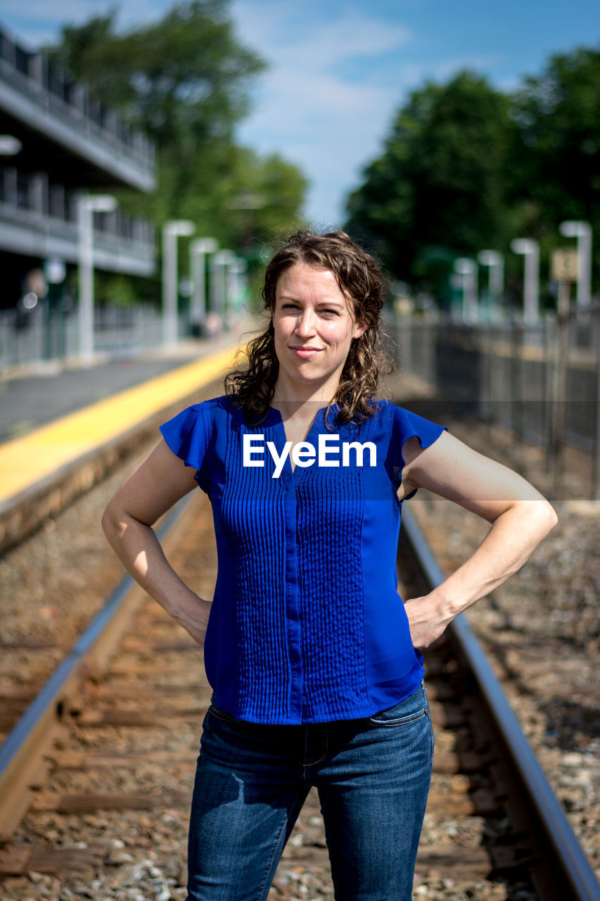 Portrait of woman with hands on hip while standing at railroad track