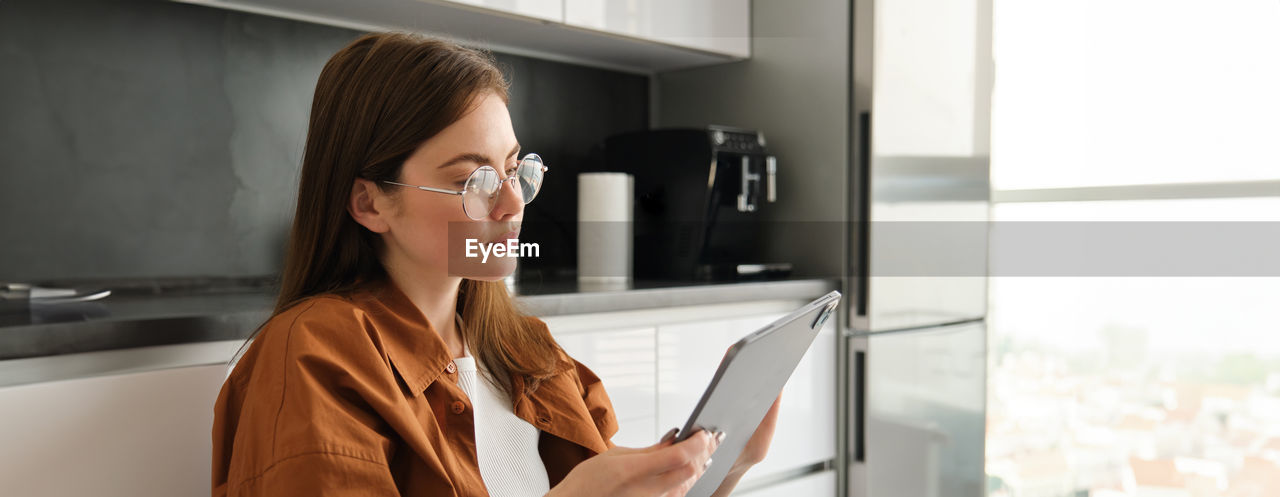 portrait of young woman wearing sunglasses while standing by window