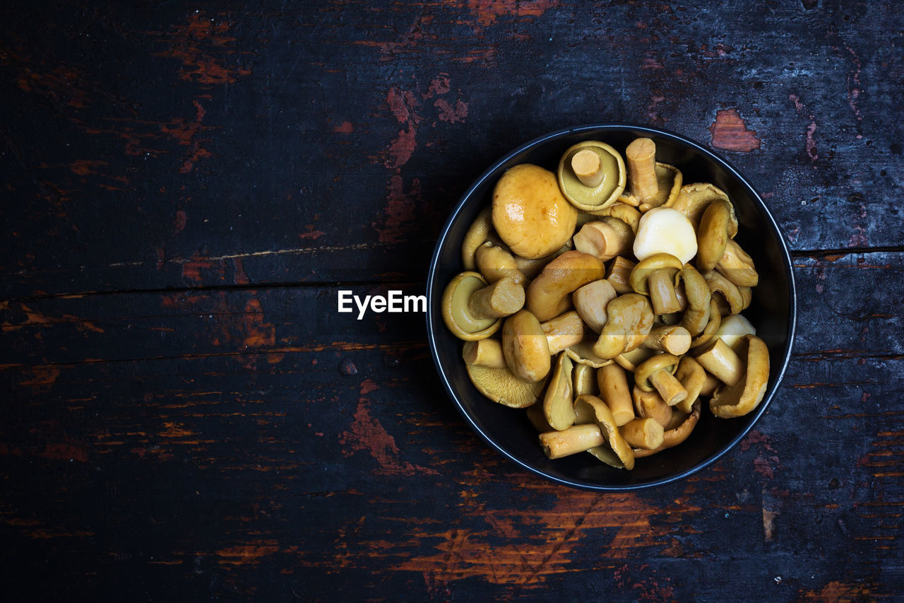 Salted milk mushroom in a black bowl on a black wooden table with a copy space top view