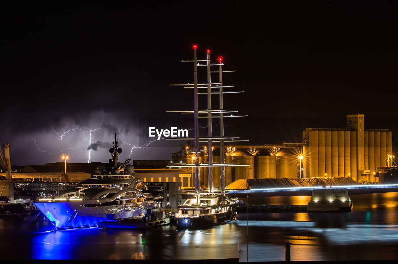 Sailboats moored at harbor against sky at night