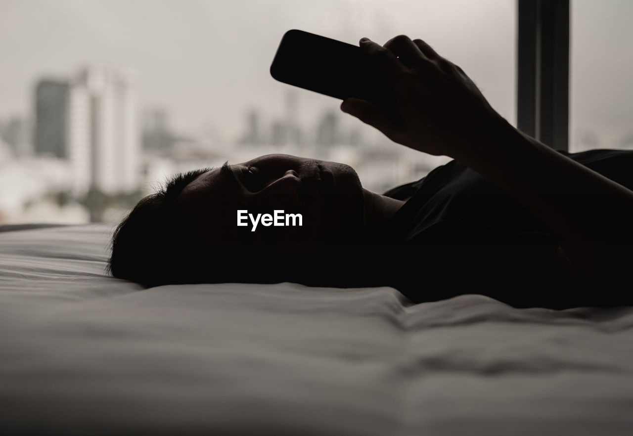 Asian man feels sad on bed looking and focus on smartphone. mental health concept.