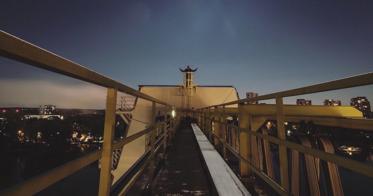 FOOTBRIDGE OVER ILLUMINATED CITY AGAINST SKY