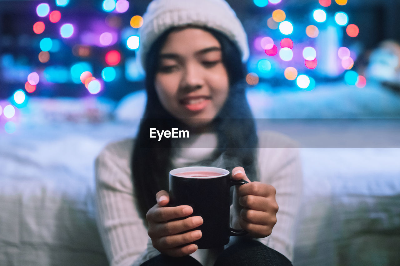 Young woman having coffee against illuminated lights