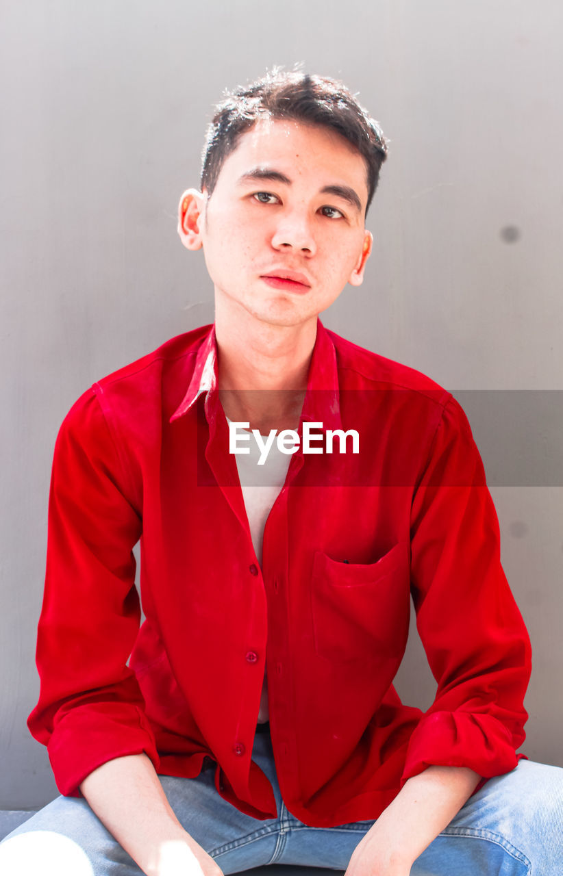 Portrait of young man sitting against wall