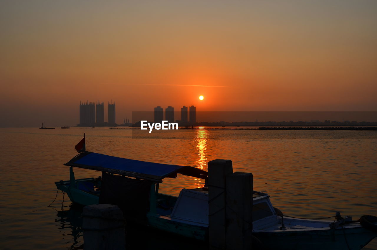 SCENIC VIEW OF SEA AGAINST BUILDINGS DURING SUNSET