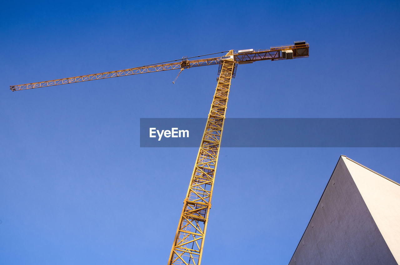 LOW ANGLE VIEW OF CRANE AT CONSTRUCTION SITE AGAINST BLUE SKY