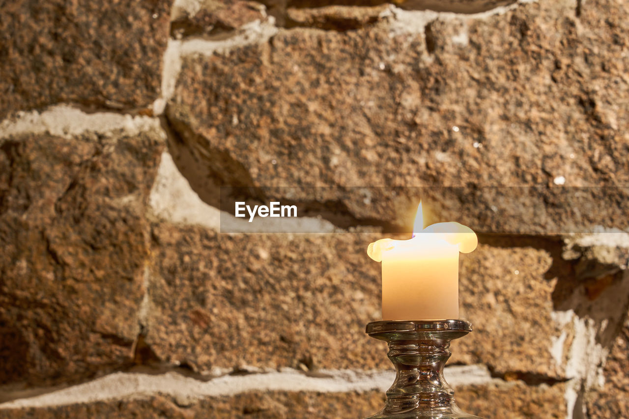 CLOSE-UP OF BURNING CANDLE AGAINST WALL