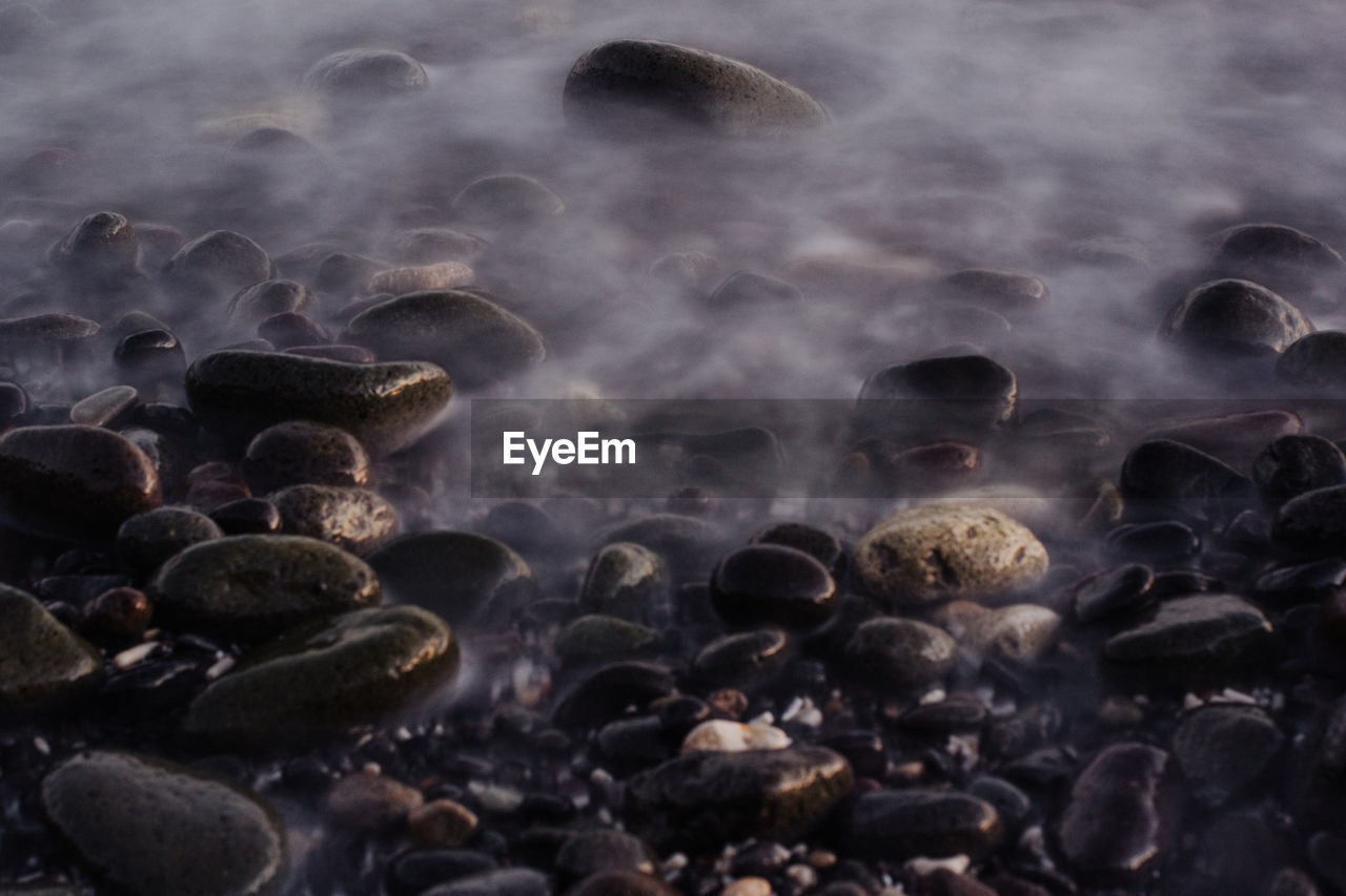 HIGH ANGLE VIEW OF STONES ON WET SHORE