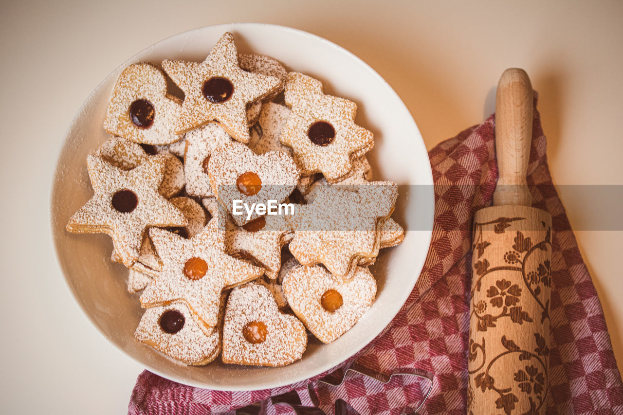 High angle view of the bowl of linzer cookies against a table cloth and a dough roller