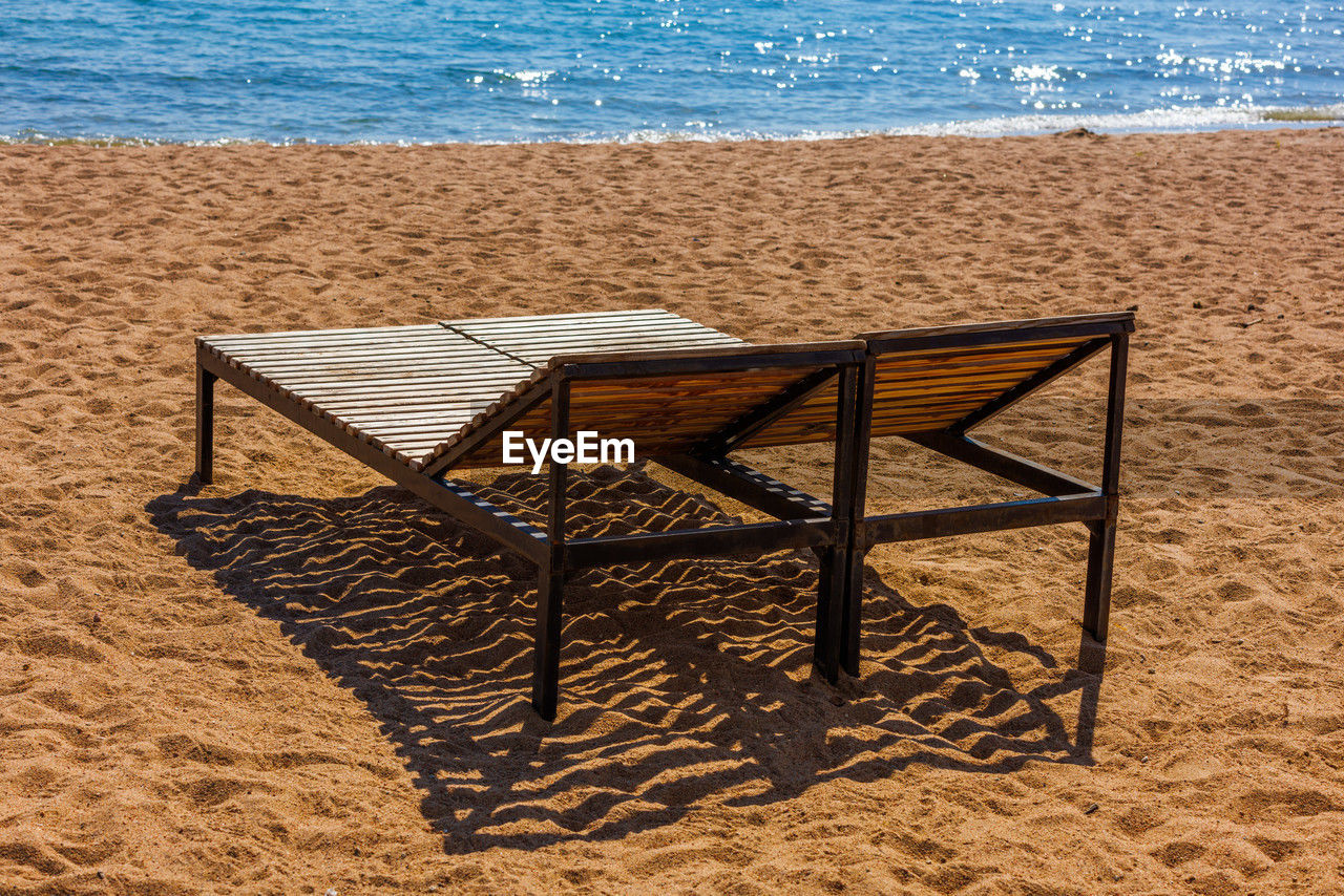 land, beach, sand, sea, water, nature, chair, no people, seat, sunlight, day, furniture, wood, beauty in nature, tranquility, tranquil scene, scenics - nature, horizon over water, outdoors, relaxation, holiday, vacation, absence, trip, shore, sky, summer, horizon, shadow