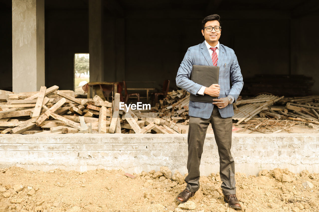 Portrait of businessman holding file standing against built structure