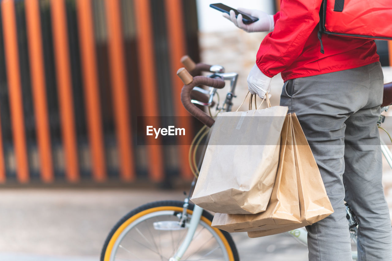 REAR VIEW OF MAN HOLDING BICYCLE ON STREET