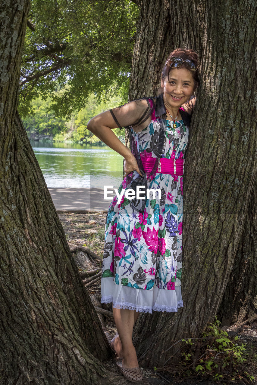 Portrait of smiling woman standing by tree trunk in forest