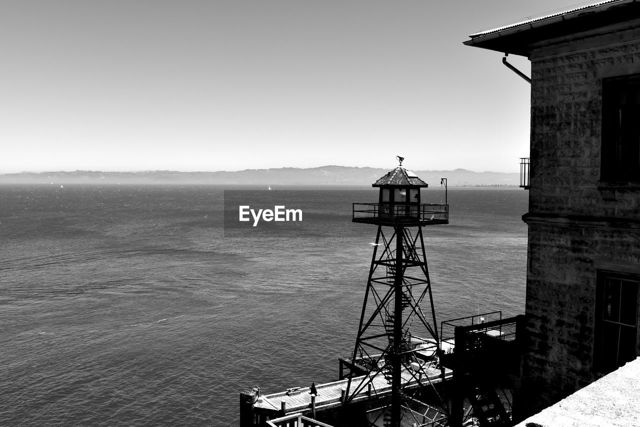 Lighthouse and building by sea against clear sky