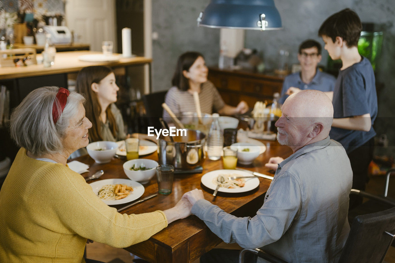 Smiling senior couple holding hands while having dinner with family at home