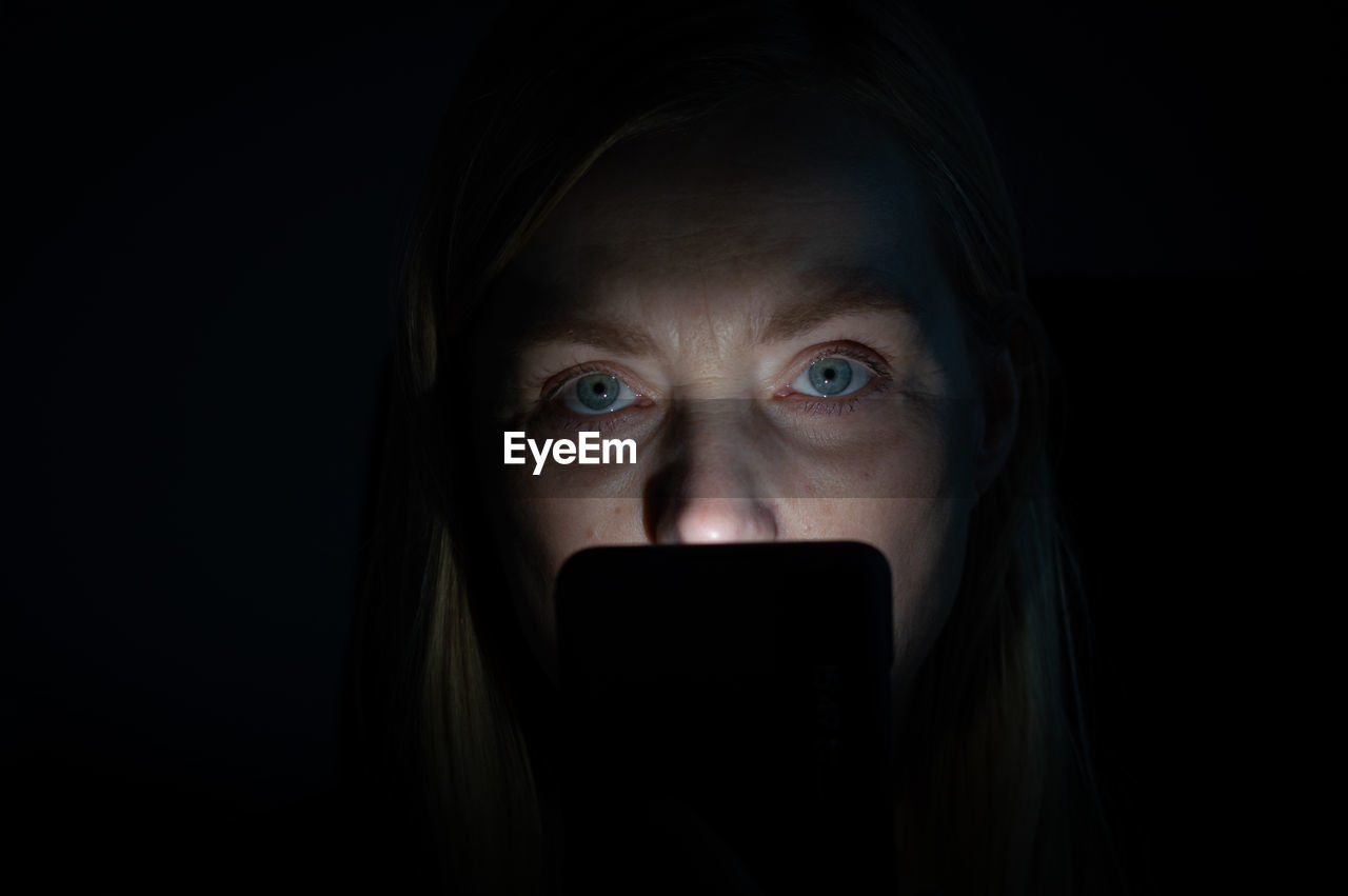Close-up portrait of woman using phone in dark