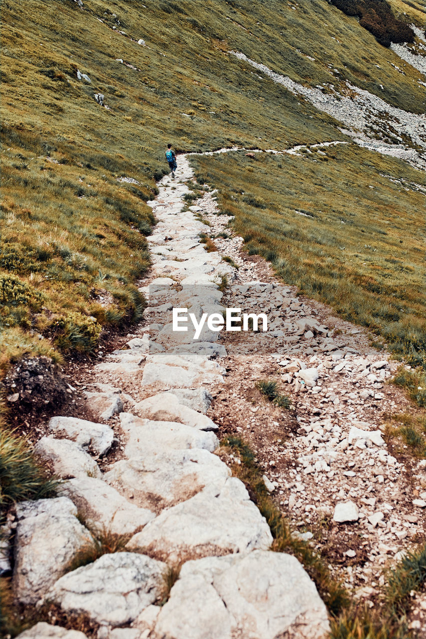 Young man with backpack hiking in a mountains, actively spending summer vacation