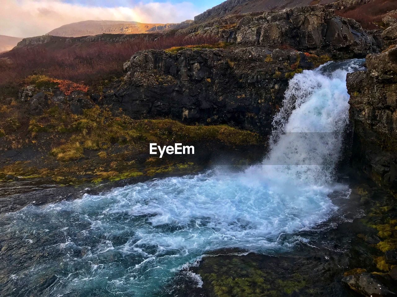 SCENIC VIEW OF WATERFALL AGAINST MOUNTAINS