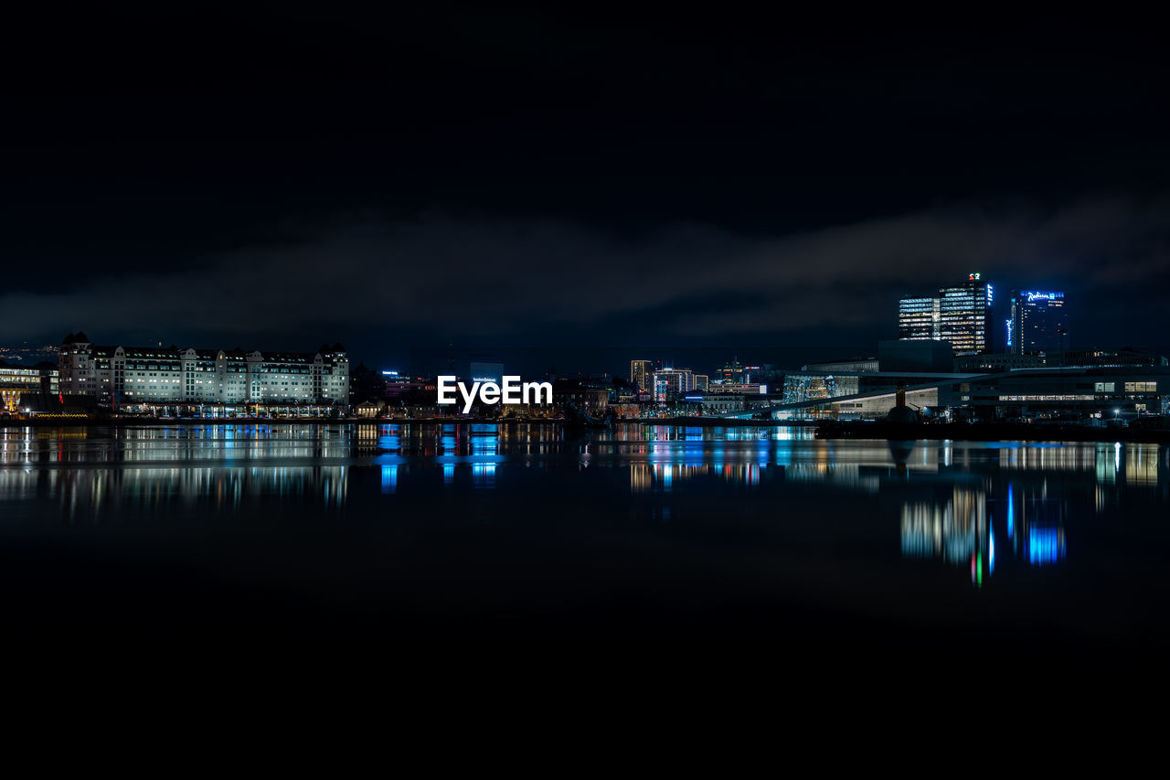 Illuminated buildings by river against sky at night