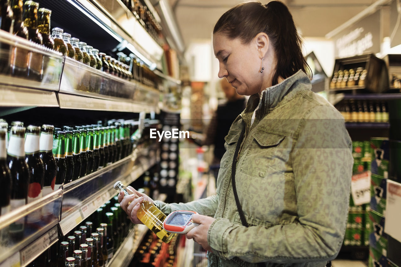 Side view of woman scanning beer bottle in supermarket