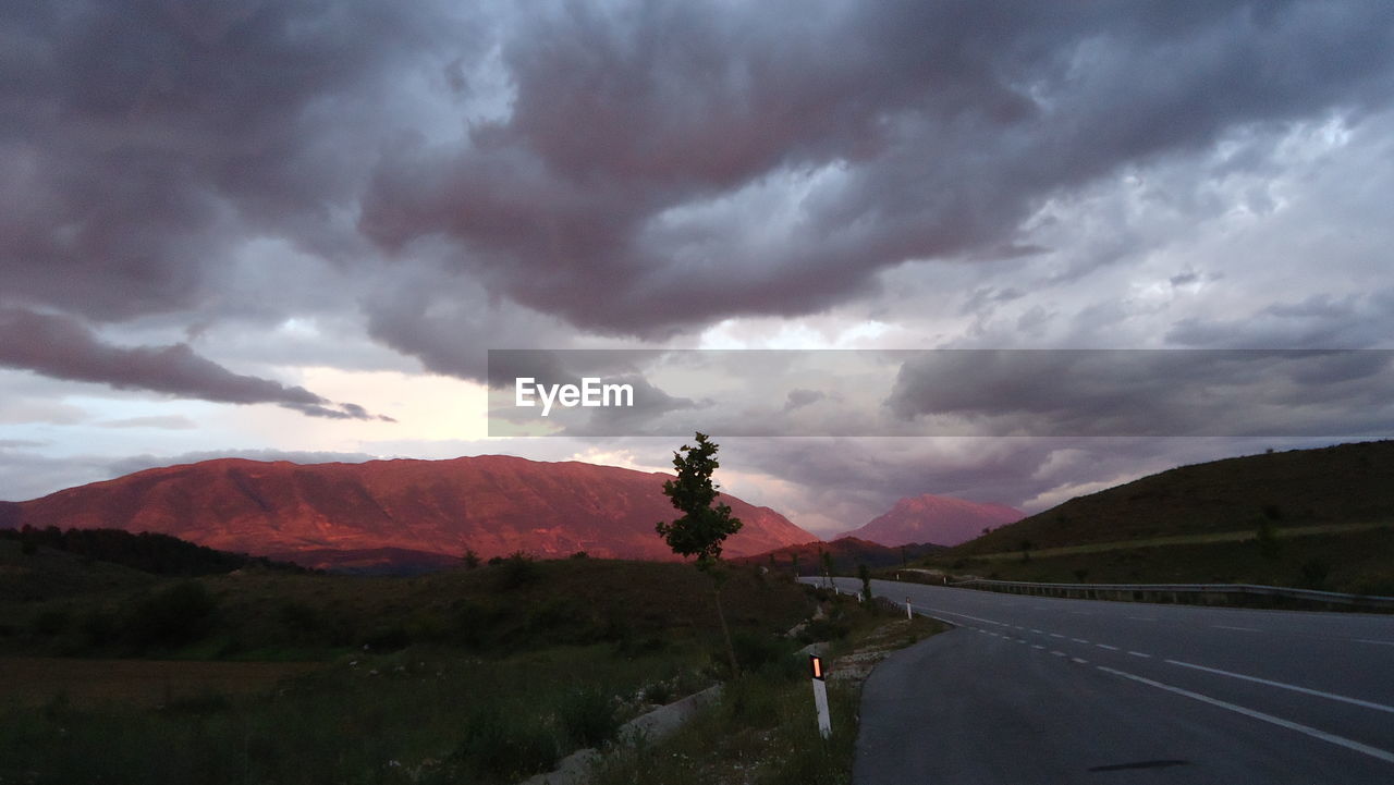 ROAD AGAINST STORM CLOUDS OVER MOUNTAINS