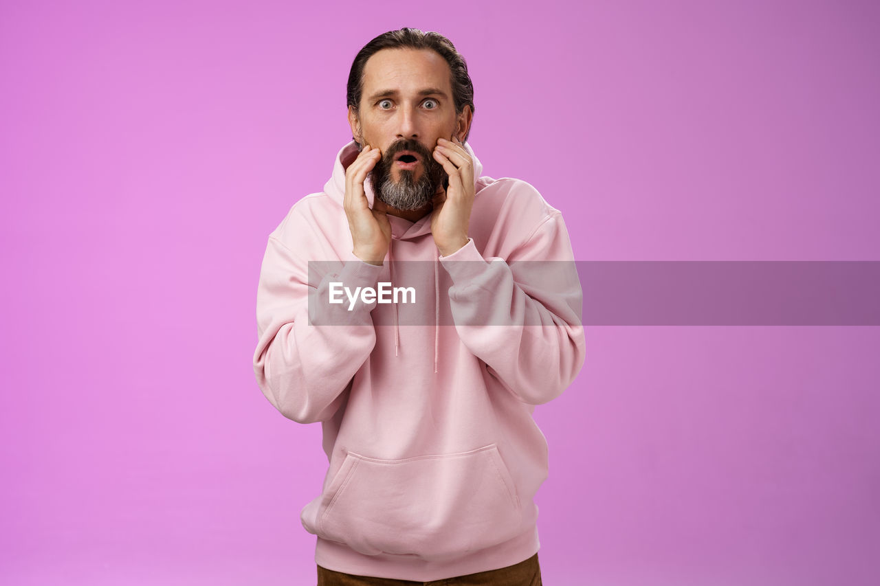 Portrait of young man standing against pink background