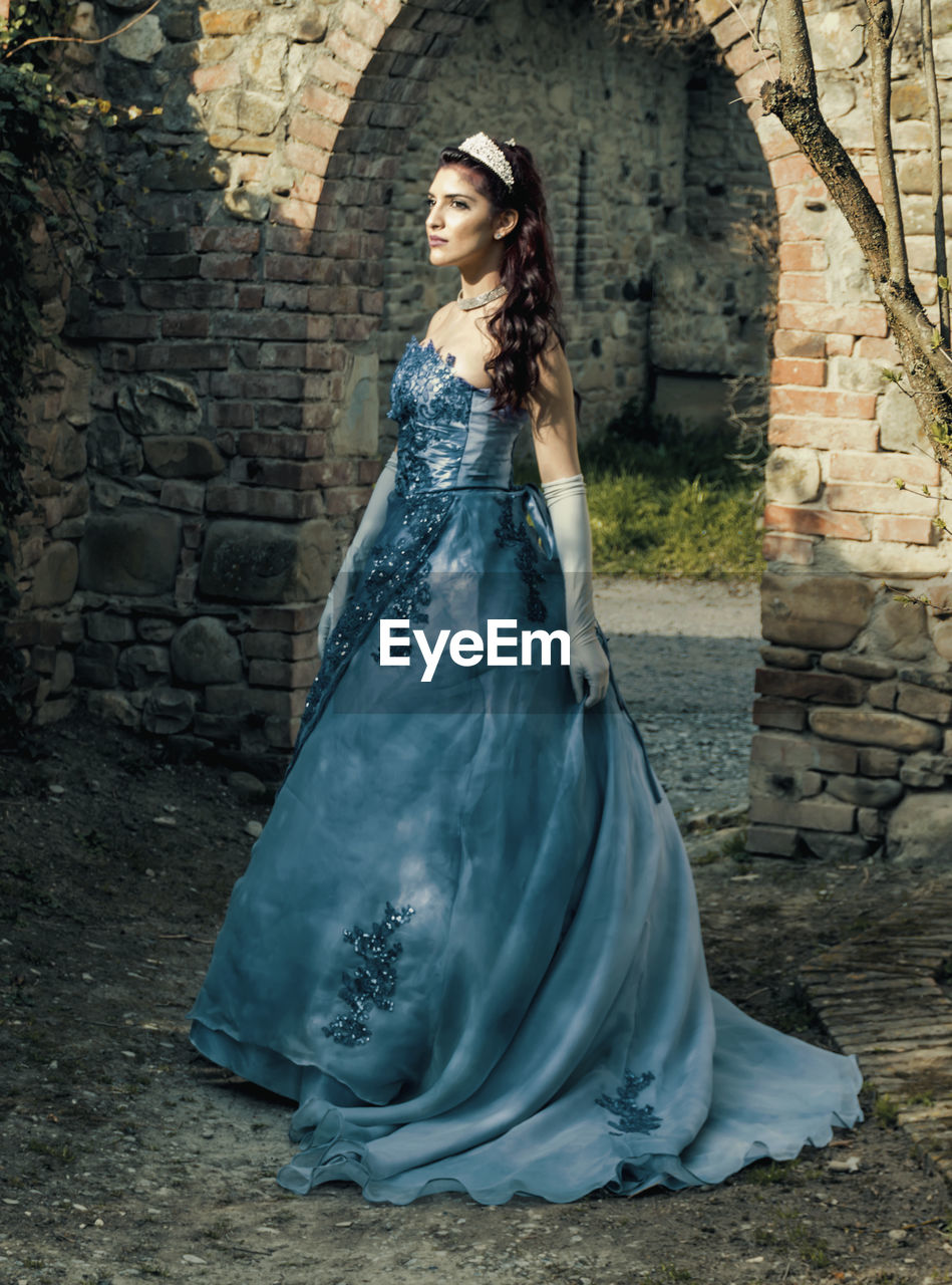 Young woman wearing evening gown while standing at old ruin