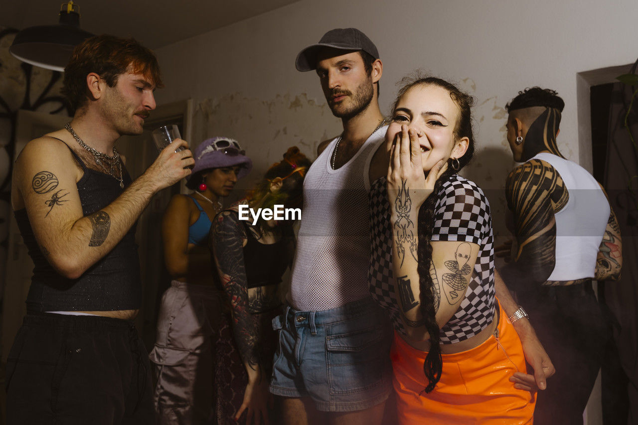 Portrait of happy non-binary person blowing kiss with friends celebrating during party in apartment
