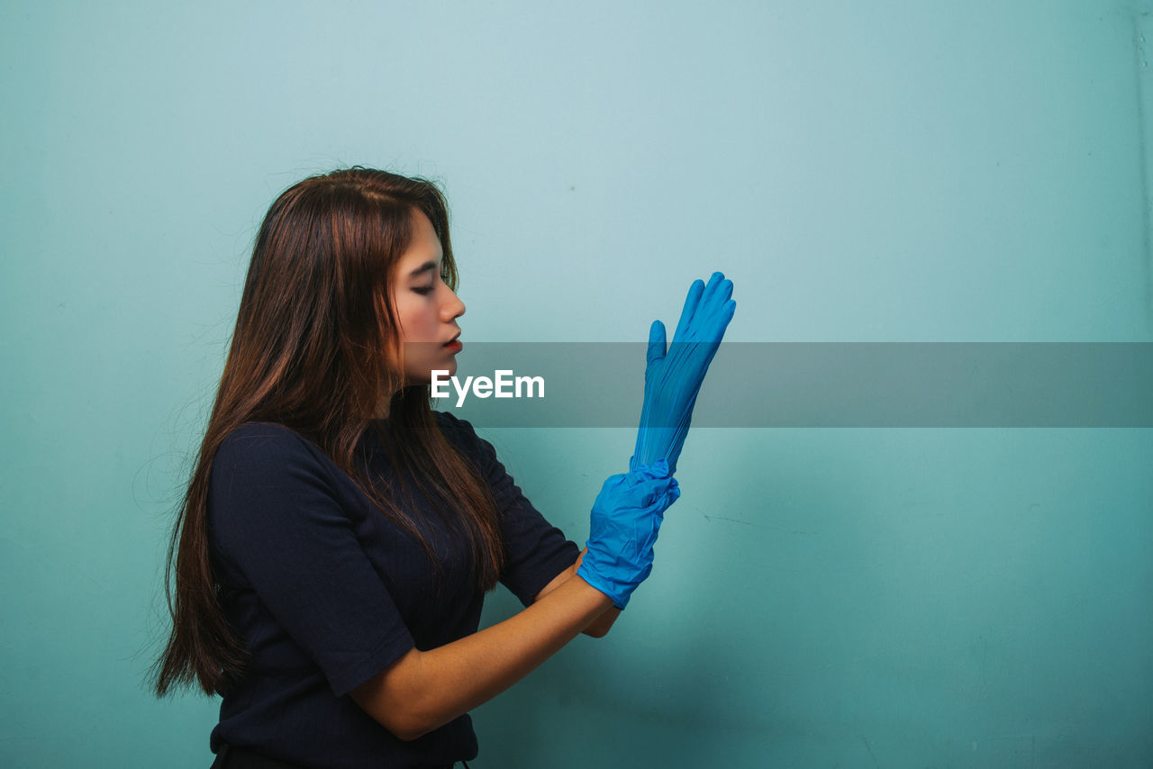 YOUNG WOMAN HOLDING BLUE HAIR AGAINST WALL