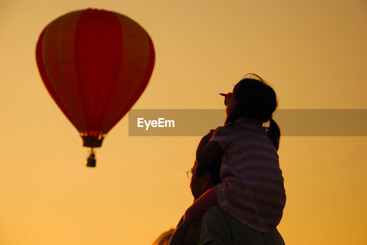 Father carrying daughter with hot air balloon against clear sky