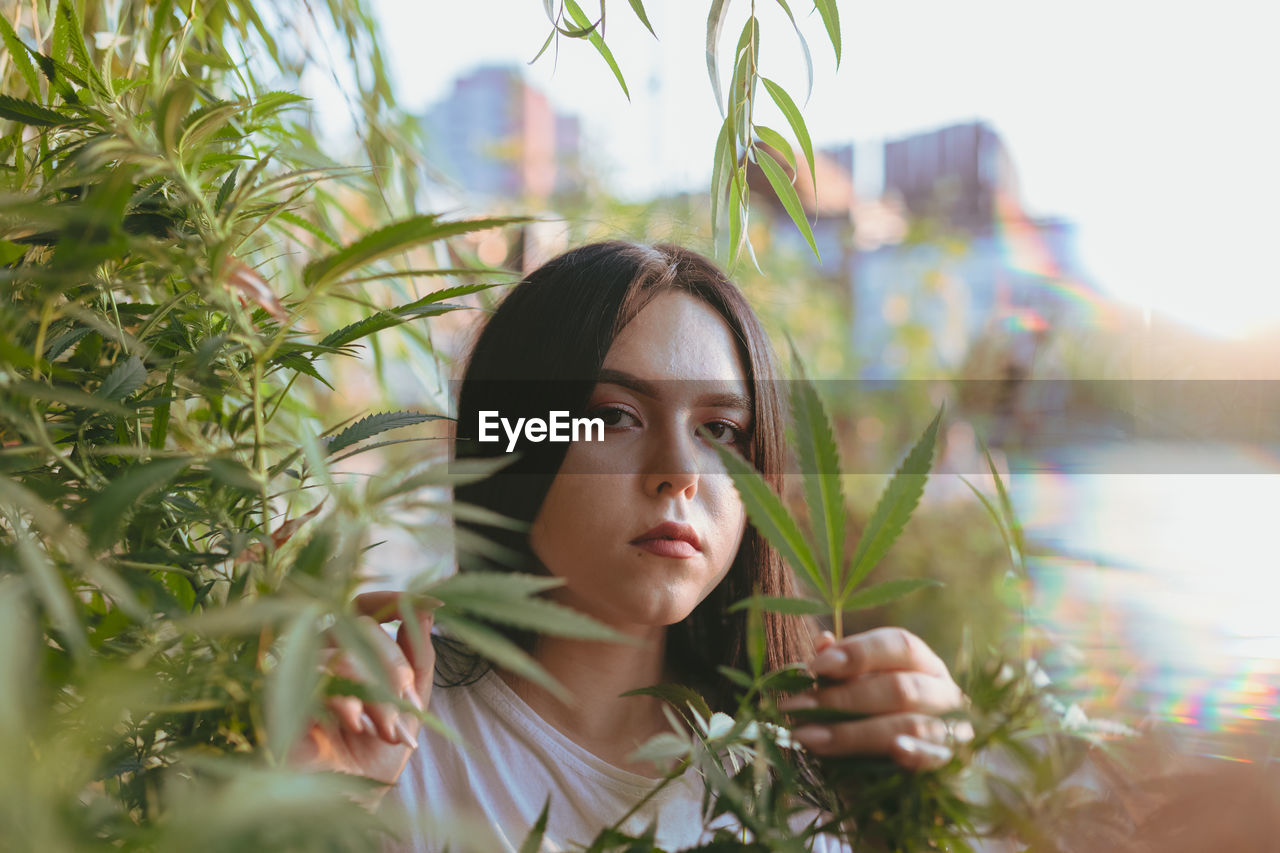 Portrait of young woman holding leaf of cannabis plant