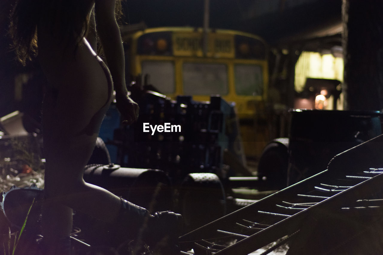 Low section of woman naked woman standing at junkyard during night