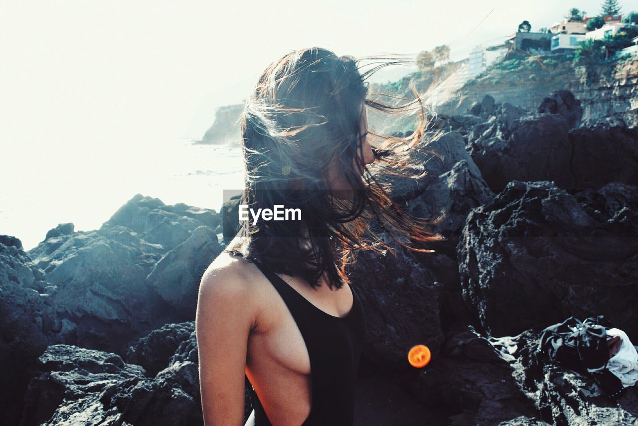 Sensuous woman with long hair standing by rocks at beach