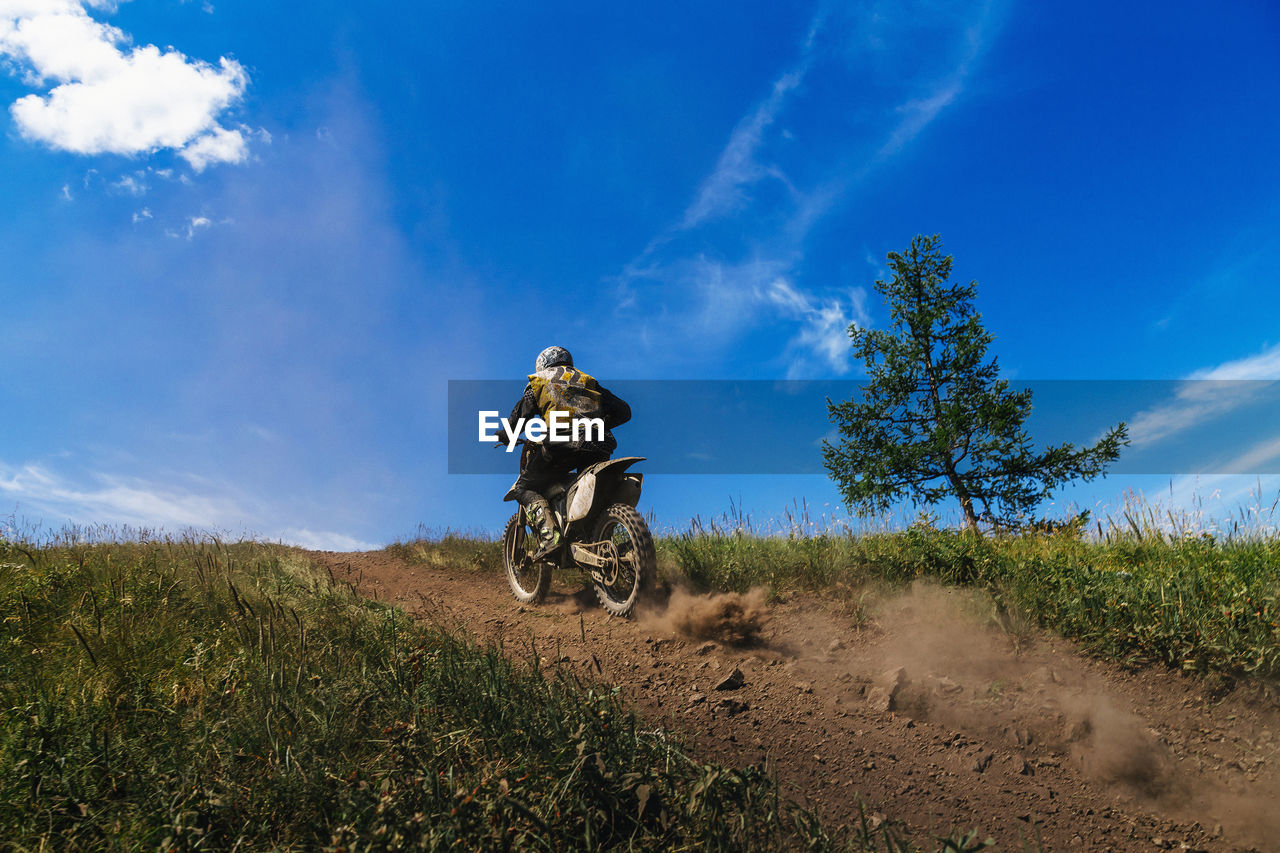 Back male biker in enduro motorcycle riding on mountain trail