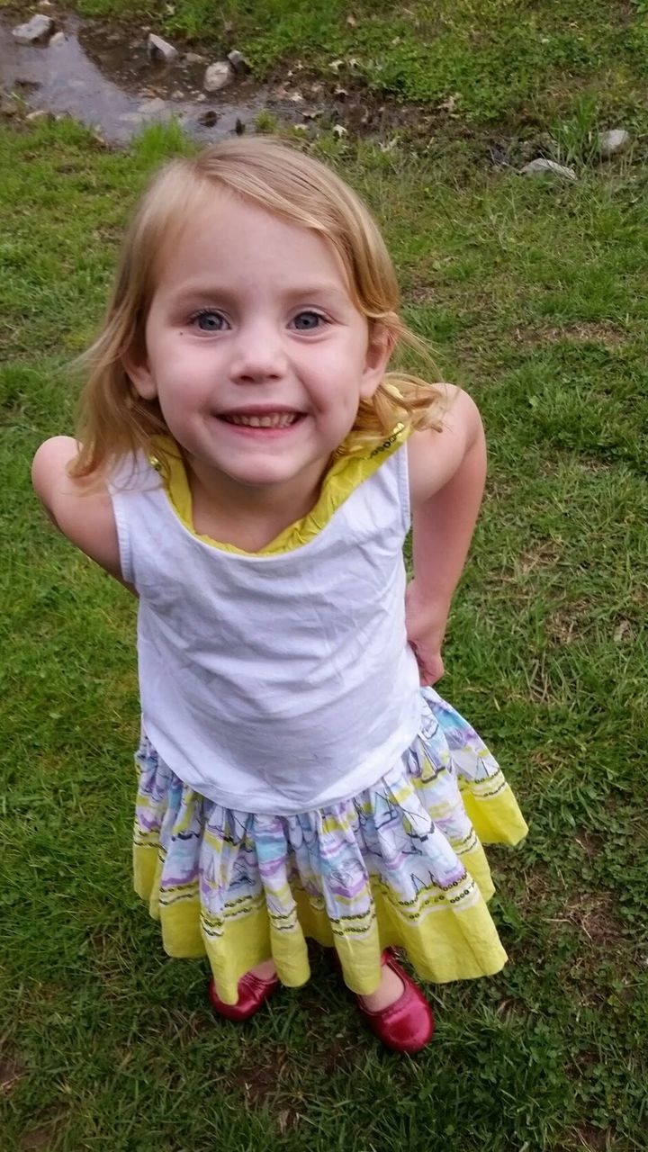 PORTRAIT OF GIRL STANDING ON GRASSY FIELD