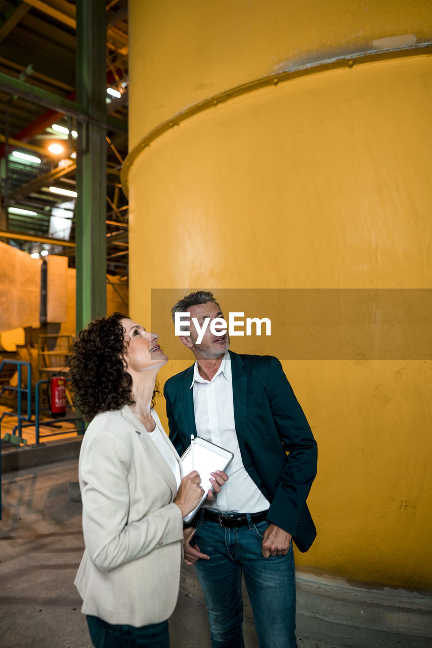 Businesswoman with digital tablet looking up while standing with colleague in industry