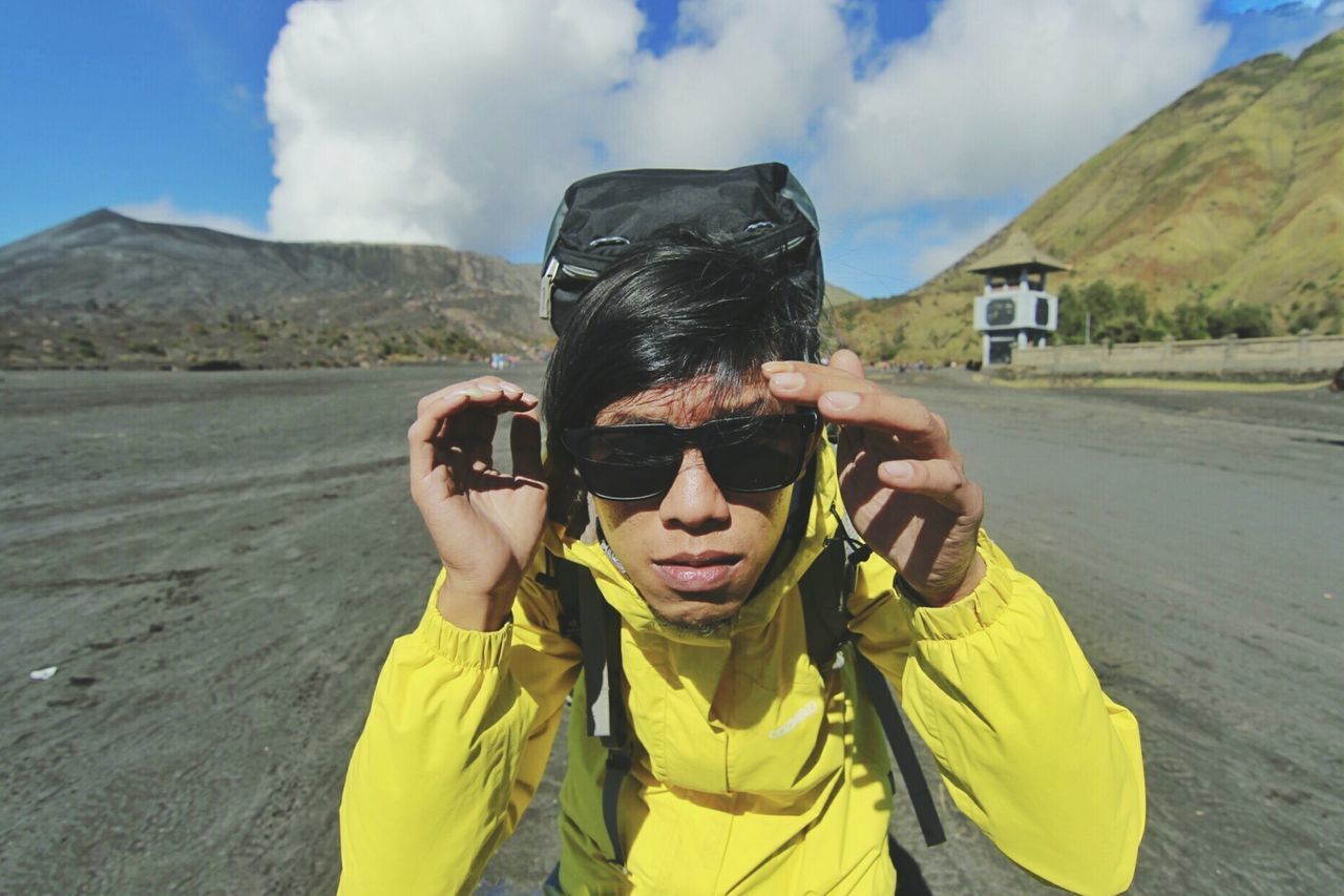 Portrait of male hiker in sunglasses standing on road against mountains