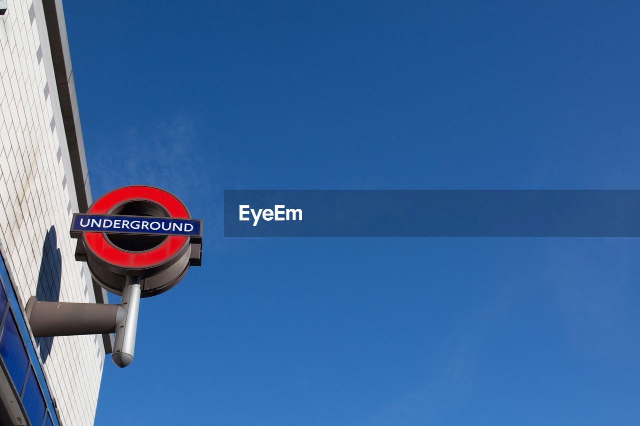 Low angle view of london underground symbol on building against clear blue sky