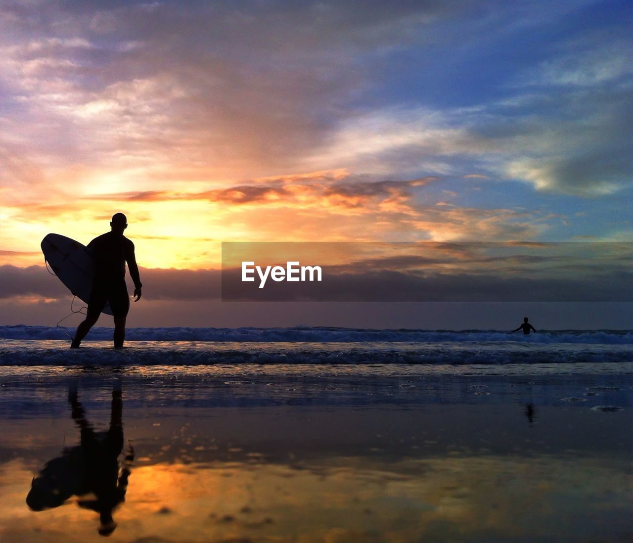 Silhouette of surfboarder walking on beach during sunset