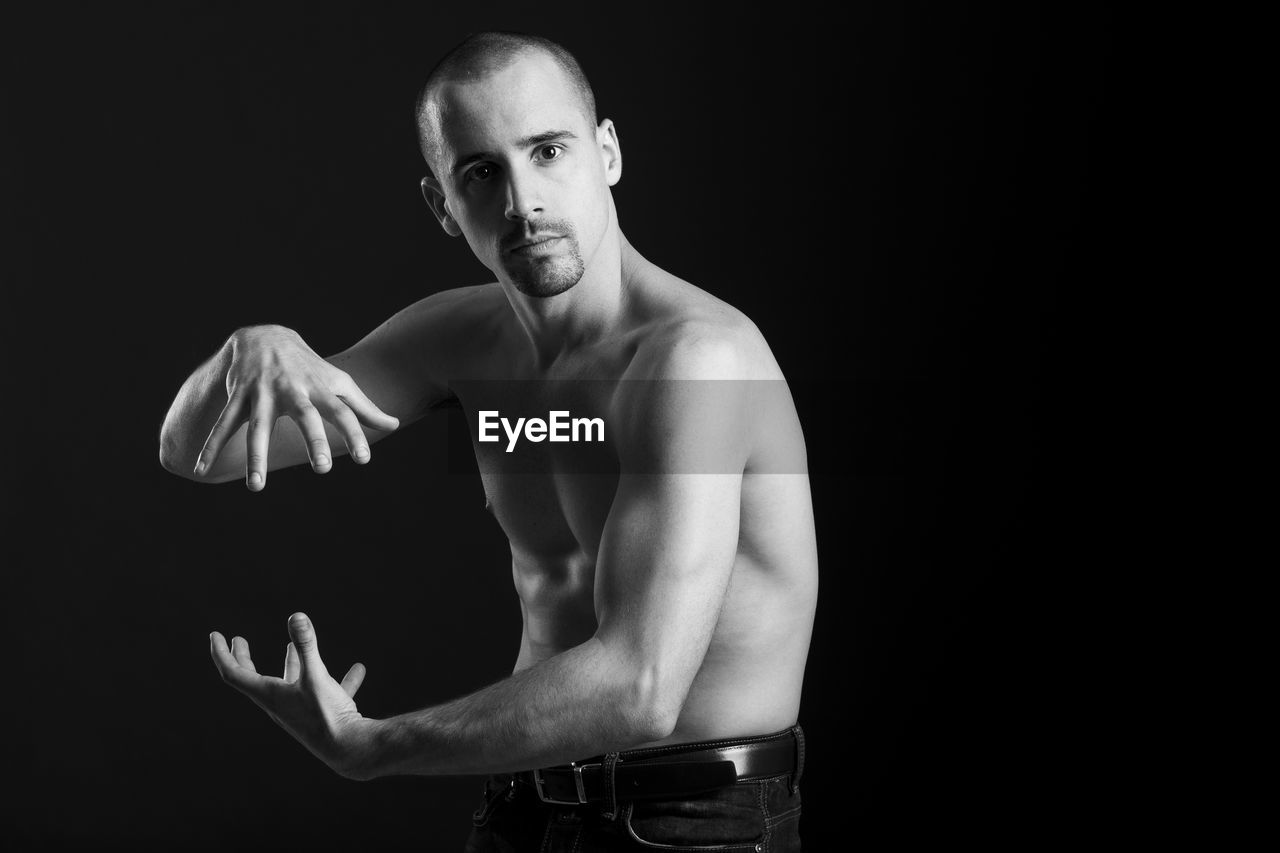 Portrait of shirtless man doing martial arts against black background