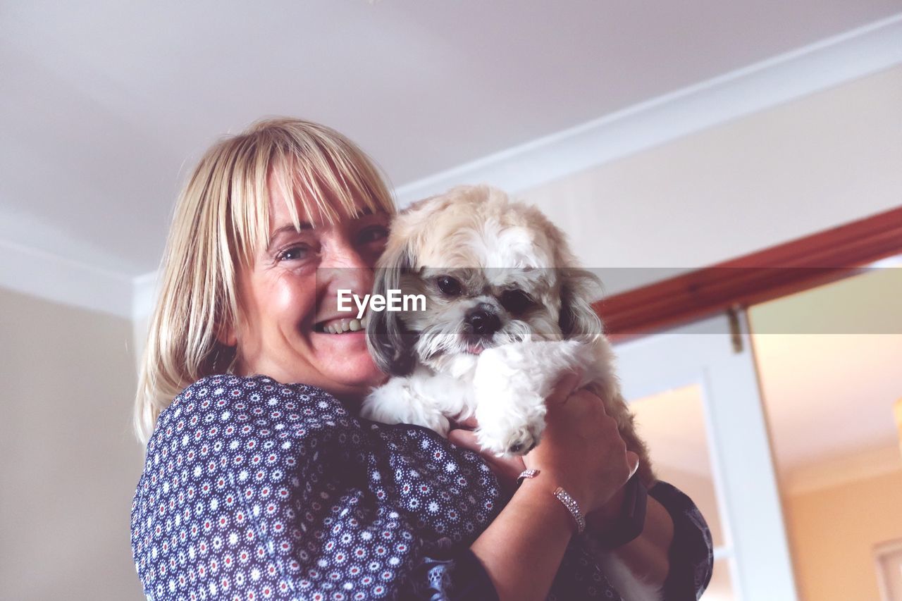 Portrait of smiling woman holding dog at home